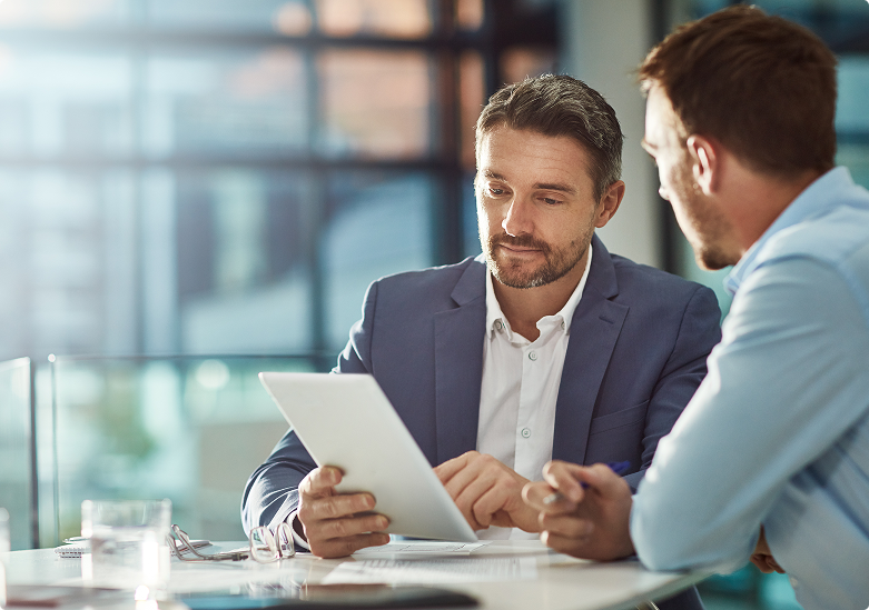 Two businessmen in a modern office reviewing documents on a tablet during a financial consultation.