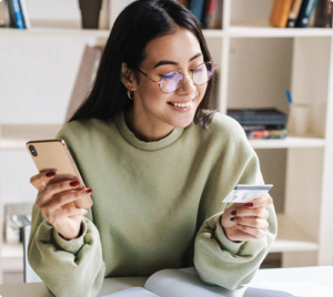 Young woman using a smartphone and holding a credit card while managing finances online at home.