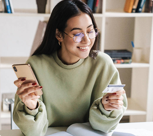 Young woman using a smartphone and holding a credit card while managing finances online at home.