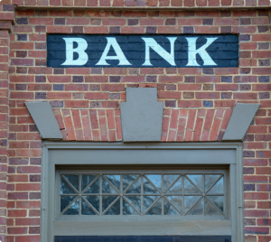 Vintage brick building with a painted ‘BANK’ sign above a window, showcasing classic architectural details.