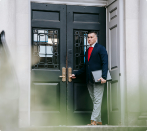 Professional man in business attire entering a historic bank building holding a laptop, symbolizing financial or consulting services.