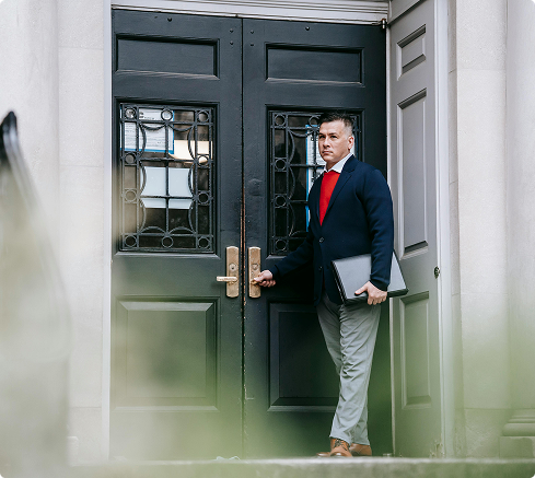 Professional man in business attire entering a historic bank building holding a laptop, symbolizing financial or consulting services.